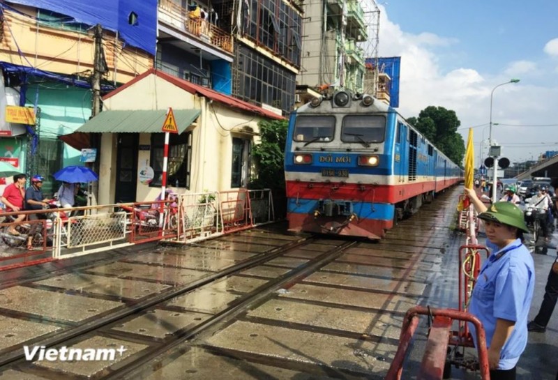 Tàu hỏa chạy qua một đường ngang có nhân viên đường sắt chốt trực tại gác chắn. (Ảnh: Việt Hùng/Vietnam+)