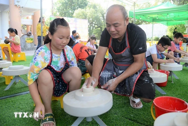 Nghệ nhân làm gốm hướng dẫn các du khách nhí vuốt, nặn gốm trên bàn xoay. (Ảnh: Anh Tuấn/TTXVN)