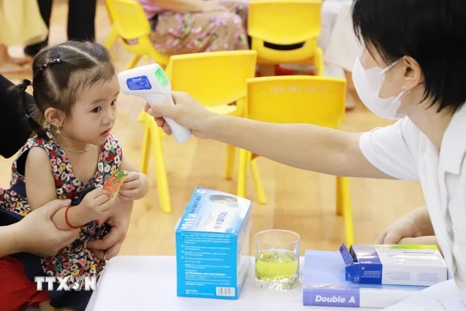 Trẻ được nhân viên y tế kiểm tra nhiệt độ cơ thể trước khi tiêm vaccine. (Ảnh: Vân Chi/TTXVN phát)