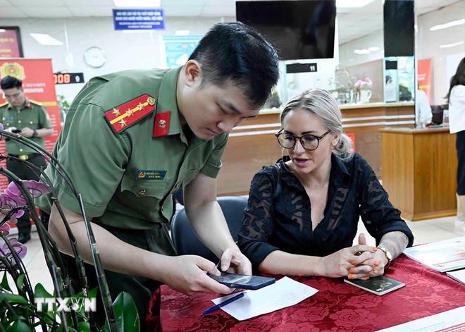 Cán bộ, chiến sỹ Cục quản lý xuất nhập cảnh, Bộ Công an hướng dẫn người nước ngoài làm thủ tục cấp tài khoản định danh điện tử. (Ảnh: Phạm Kiên/TTXVN)